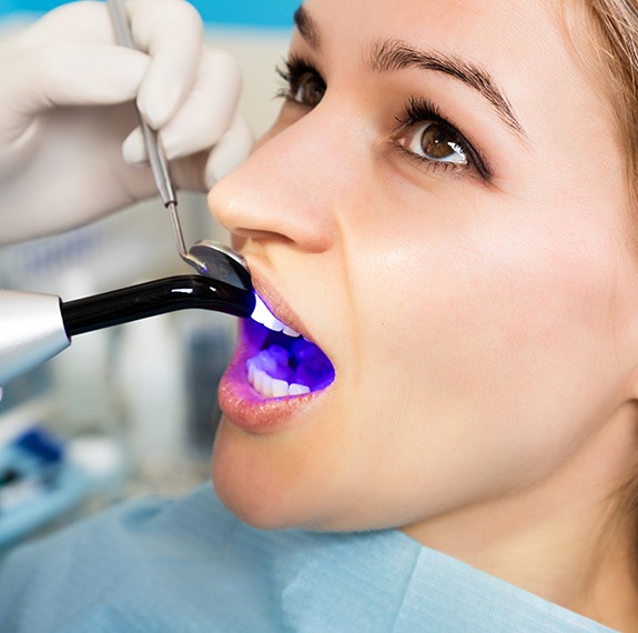 Dentist applying ultraviolet light to woman’s dental bonding