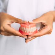 Woman in white clothing holding full set of dentures with two hands in front of her center