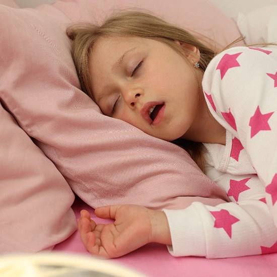 Snoring young child on pink bedsheets