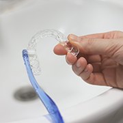 Person cleaning a clear aligner in sink