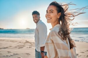 Woman and man holding hands smiling walking on the beach