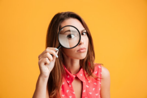 Woman on burnt-yellow background using a magnifying glass